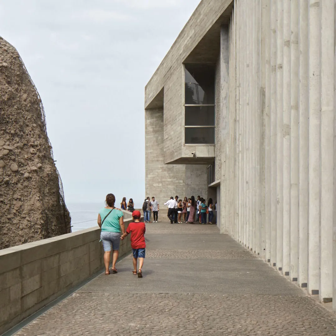 Personas caminando cerca de una estructura moderna de concreto al lado de un acantilado