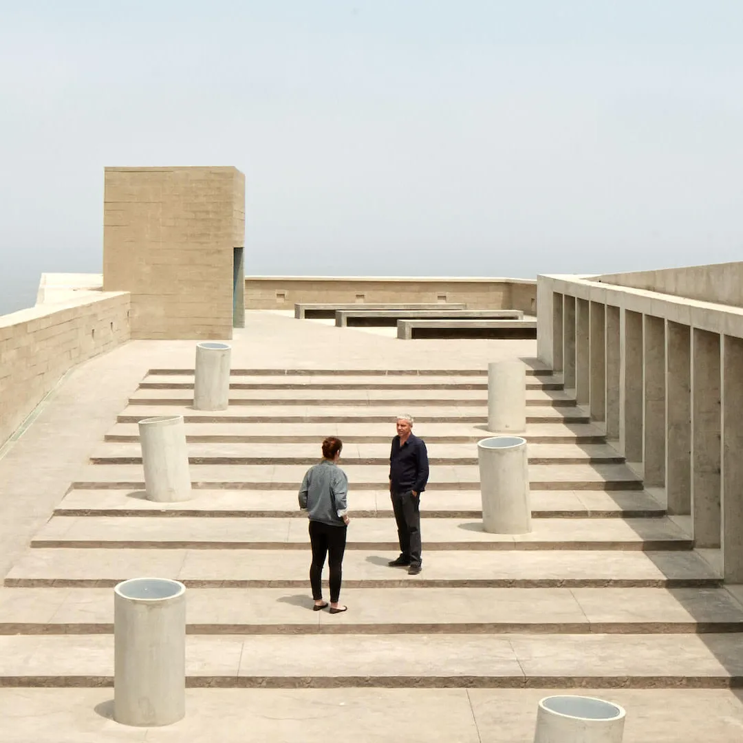Dos personas conversando en una terraza de concreto con vista al mar